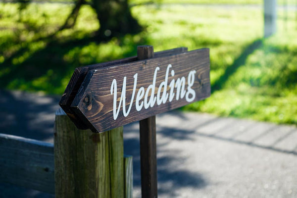 A wooden arrow sign that reads “Wedding” pointing in the direction of the event.